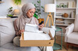 © Jovo Jovanovic/Stocksy - Woman in hijab opens box, examines product.