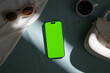 © Marc Tran/Stocksy - Flat lay of a smartphone with green screen, sunglasses, coffee and bag