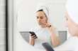 © Asya Molochkova/Stocksy - Woman Brushing Teeth While Using Smartphone in Bathroom