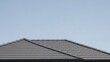 © Pemeke - Architectural detail of a modern residential roof with dark grey tiles against a clear blue sky