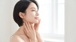 © YT - 明るい窓辺のやさしい光の中でフェイスラインから首元に手を添え、美しい横顔となめらかな肌印象を見せる若い女性のビューティーイメージ、フェイスケア・ネックケア・美容広告に適した上品で清潔感のある人物素材