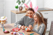 © Pixel-Shot - Cute little girl and her mother in bunny ears painting Easter eggs in kitchen