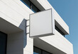 © joe - Empty white sign on modern building exterior angled against a clear blue sky. Blank signage mounted on a light-gray metal frame on the side of a modern business building.