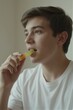 © Michael - A young man with short brown hair and a light beard sits in a modern living room, contemplating a piece of yellow candy as soft natural light filters through the window.