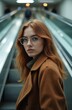 © Viktor - Redhead woman wearing glasses and brown coat on escalator. She looks at camera with calm expression, ready for journey. Modern transport hub scene.