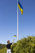 © Anna - adult girl proudly holds small Ukrainian flag while standing under a large, high-raised flag. stand with Ukraine. National identity. Independence Day. Freedom, trust, pride, national symbol. Stop war