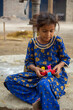 © FerozAli - Little girl playing with toy while sitting on ground in rural village simple childhood lifestyle scene