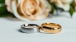 © savittree - Elegant silver and gold wedding rings positioned elegantly beside a soft rose flower on a white background