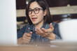 © tippapatt - Woman wearing glasses gestures while speaking during online meeting, focused at laptop in modern indoor workspace, video conference, online business, close up