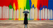 © JANSSENS LUCAS DAAN - Woman in black dress holding umbrella before a rainbow paint drip wall. Rear view of person standing in front of vibrant urban mural. Creativity, diversity, and protection concept for marketing.