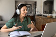 © fizkes - Woman in headphones speaks during video call, remote coaching at home office sits at table with laptop and notebook in living room. Online coaching, tutoring, consulting services, videoconferencing