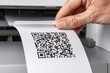 © whitestorm - Close-up of a hand pulling a printed QR code from a printer, symbolizing digital information and technology.