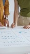 © rogerphoto - Business professionals reviewing financial charts, calculating data with calculator on table, analyzing statistics during collaborative project meeting, close up vertical view