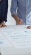 © rogerphoto - Business colleagues are examining financial data, pointing at charts and graphs spread out on a table during a collaborative analysis session in a modern office.