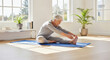 © __arygraphicart - Elderly woman practicing yoga and stretching on a mat in a bright, sunlit room, promoting health and wellness