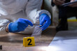 © Dejan - Forensic specialist in protective suit and blue gloves collecting evidence with tweezers at a marked crime scene, assisting investigation