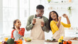 © Prostock-studio - A family stands in a bright kitchen preparing food together. The father shares a laugh with his daughter, while the mother watches them joyfully. Fresh vegetables and dishes are on the counter.