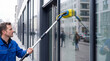 © Olesya - Window cleaner washing commercial building glass with water fed pole. Professional janitor cleaning facade of office store. Service industry occupation, hygiene and maintenance concept.