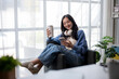 © apichat - Young Woman Enjoying Coffee While Using Smartphone at Home