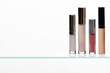 © vasanty - Different vertical cosmetic tubes likely lip gloss, liquid foundation, or concealer with metallic gold and silver caps, neatly arranged on a reflective glass shelf.
