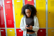 © Halfpoint - Student standing in school locker room, looking at phone.