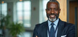 © Viktor - Smiling Black man in suit stands in modern office. Mature pro with beard has lanyard. He looks successful and confident. Career growth and leadership concepts.
