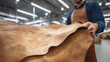 © Katerina Bond - A craftsman in a leather apron inspects a large piece of brown leather in a factory workshop. Selective focus.