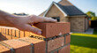 © Sohail - A hand placing a brick on top of a brick wall in a residential area