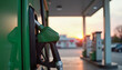 © KIRA POSLAVSKAIA - Green fuel nozzle on pump at gas station during sunset background