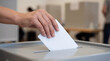 © Galina Petrova - Hand placing a paper ballot into a box at a polling station, representing civic participation, voting process, election procedures, public governance, and democratic decision making.