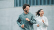 © Andrey - Man and Woman in Activewear Jogging Together Outdoors in a City Environment with Modern Concrete Walls and Clear Daylight Setting