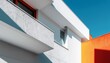 © Bayu - A modern building with white and orange walls features balconies under a clear blue sky
