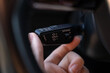 © Marina - Close-up of hand using cruise control stalk in modern car, showing speed setting and distance adjustment controls on steering column lever.