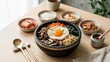 © 현욱 김 - 돌솥 비빔밥과 신선한 채소, 계란, 고추장, 다양한 반찬이 어우러진 건강한 한식 식사