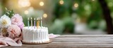 Celebration setup with birthday cake, colorful candles, flowers, and warm sunset lighting on a wooden table in an outdoor setting