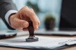 © Daniel - Corporate employee applying stamp to official document in office setting, illustrating business approval process, administrative workflow, and professional paperwork management.