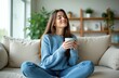 © Oleksandr - Woman with closed eyes enjoys coffee aroma while sitting cross-legged on a sofa. She holds a light blue cup, breathing in the warm scent of her beverage.