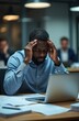 © Oleksandr - Black man holds head in hands with eyes closed, feeling stressed at office desk. Tired businessman works late on laptop with paperwork, suffering from mental strain and fatigue.