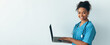 © Prostock-studio - A nurse stands in an office space with a laptop in hand, smiling. She wears scrubs and a stethoscope, ready to assist patients and manage tasks using technology.