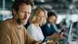 © pattozher - Focused Endeavor: A focused individual engages with technology within a professional environment, engrossed in their work alongside colleagues.