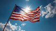 © iconic - The American flag is backlit by the sun, creating a dramatic silhouette against a cloudy blue sky.