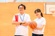 © buritora - A male teacher who is the club advisor and a female student holding a basketball are in the gymnasium.