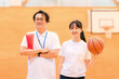 © buritora - A male teacher who is the club advisor and a female student holding a basketball are in the gymnasium.