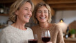 © forenna - Two women in their 50s laughing over wine in upscale kitchen, midlife female friendship, empty nesters, reinvention through community, spring entertaining, affluent home, women over 50, social recon