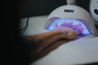 © qunica.com - Hand undergoing a gel manicure cure under a UV LED lamp. A close-up view of fingers receiving a glossy pink nail polish treatment in a salon setting.