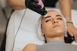 © qunica.com - Woman lying with eyes closed while an esthetician applies a facial treatment using a handheld device at a beauty center. A close-up view of a skincare session showing calm, professional care.