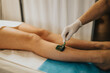 © qunica.com - Leg waxing treatment at a beauty center with a gloved esthetician applying green wax to a client. Close-up of the waxing procedure on lower legs in a spa setting.