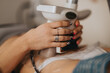 © qunica.com - A woman holds a handheld body-contouring device against her abdomen during a cosmetic treatment at a beauty center. The close-up shows hands, nail art and rings as the noninvasive slimming procedure.