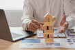 © ArLawKa - The image depicts a businessman building a tower from wooden blocks, illustrating the concept of business strategy and planning for success.