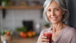 © Laura - Faceless smiling senior woman standing in a kitchen enjoying a red fruit juice for a senior wellness and nutrition concept. Defocused kitchen background. Senior red juice, kitchen